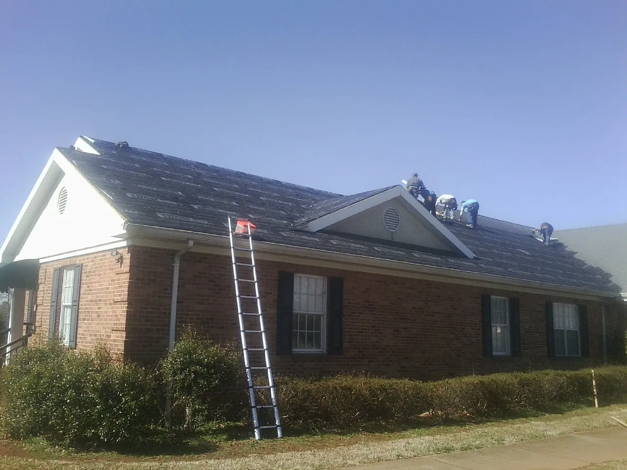 Crew tearing shingles off a brick ranch roof with a ladder set — Metal Roof Repair work by our crew in West Columbia