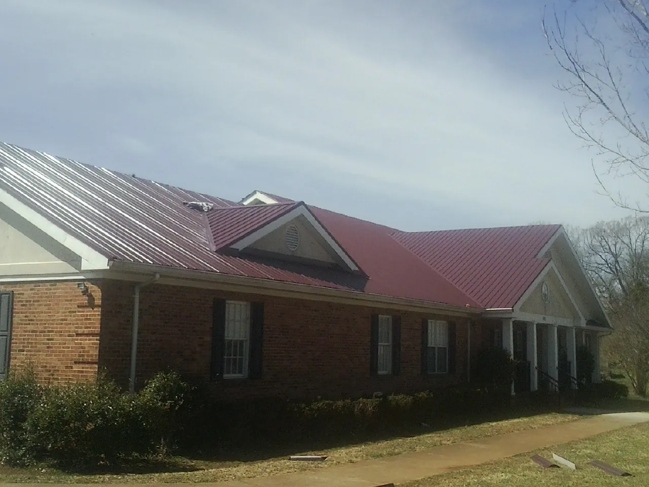 Red metal roof with gabled entries on a long brick building, from a Hail Damage Roof Repair job in West Columbia